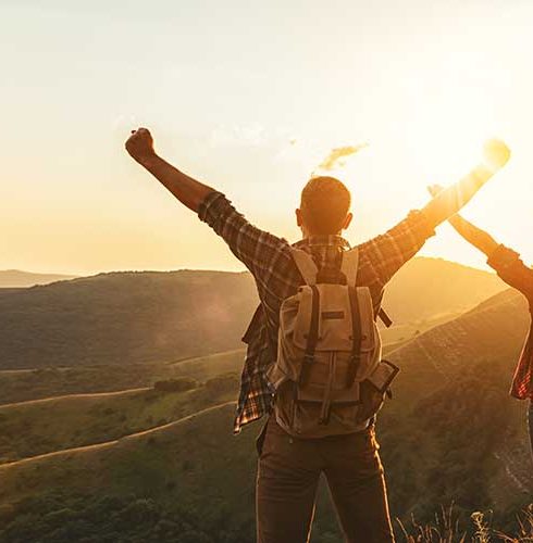 happy couple man and woman tourist at top of mountain at sunset  in summer