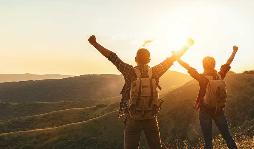happy couple man and woman tourist at top of mountain at sunset  in summer