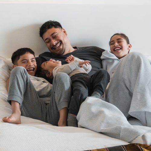 Dad and 3 children sitting on hotel bed laughing